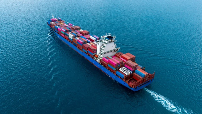 Containerschiff fährt über offenes Meer und transportiert zahlreiche bunte Frachtcontainer auf seiner Deckfläche.