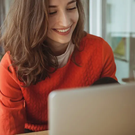 Person mit rotem Oberteil sitzt am Laptop und berechnet ihre Sparpläne.
