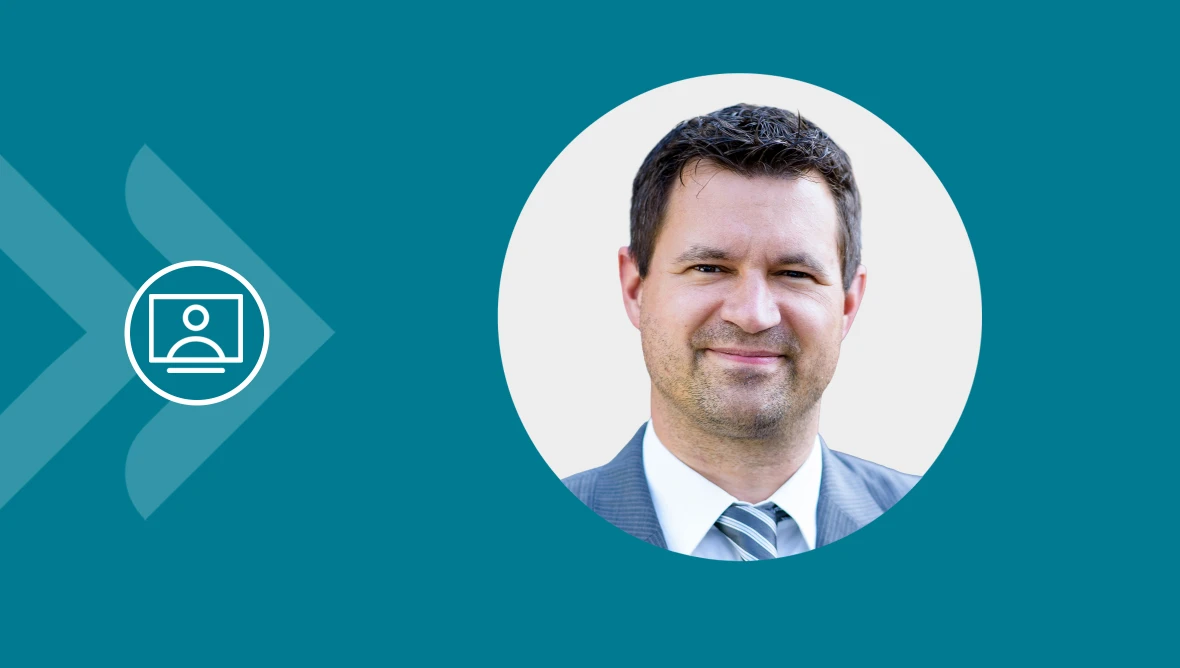 Eine geschäftlich gekleidete Person in kreisförmigem Portrait vor türkisfarbenem Hintergrund mit Video-Symbol.